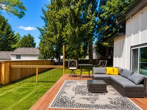 A backyard with a wooden deck, outdoor furniture, and a large tree. - 3-bedroom house in Vancouver with large yard and AC to relax (Vancouver)