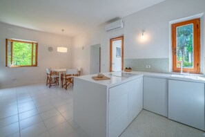 A modern kitchen with white cabinetry, a central island, and a dining area with a table and chairs. - Villetta Olea - Goelba (Portoferraio)