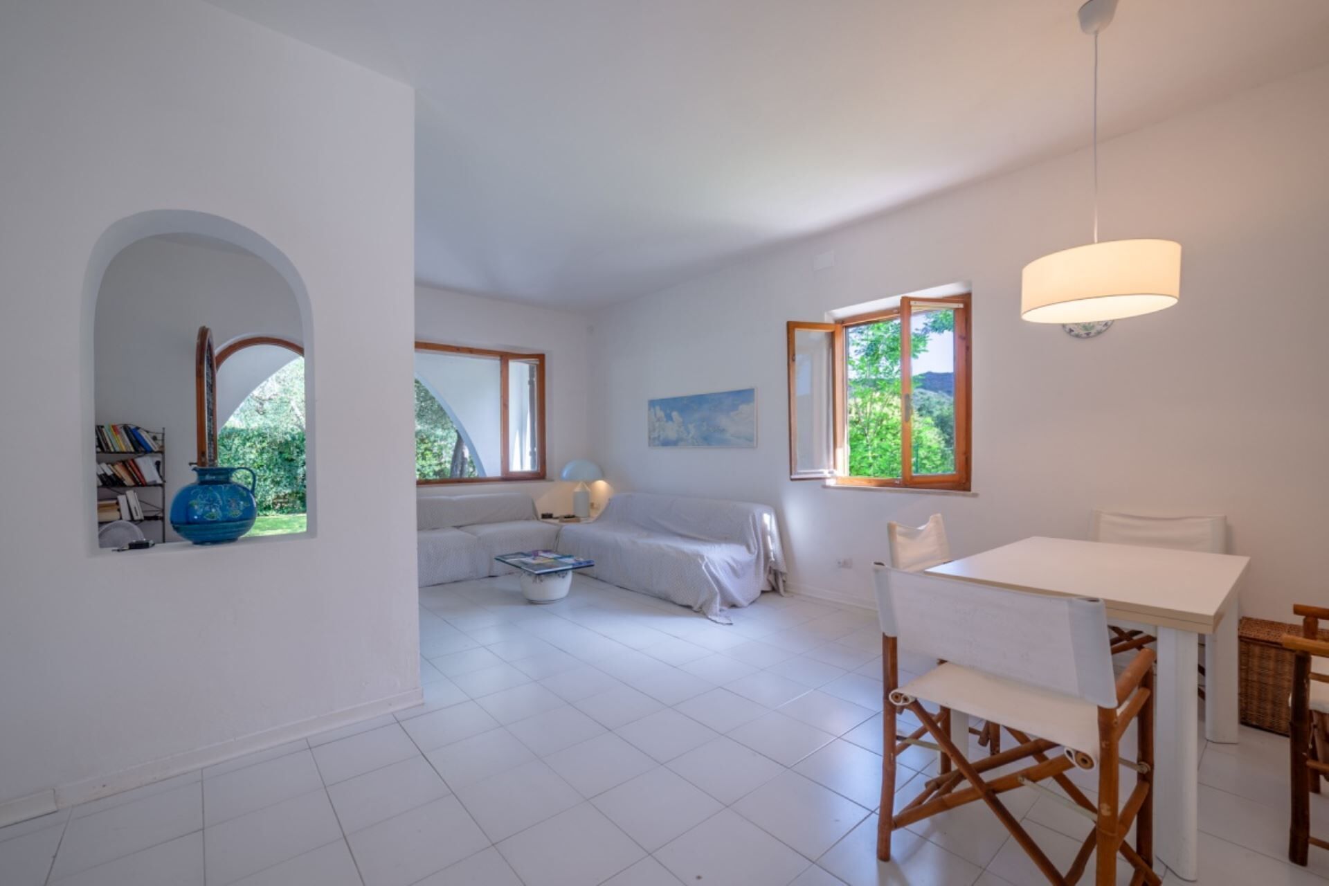 A spacious room with a white sofa, a dining table, and a large window.
