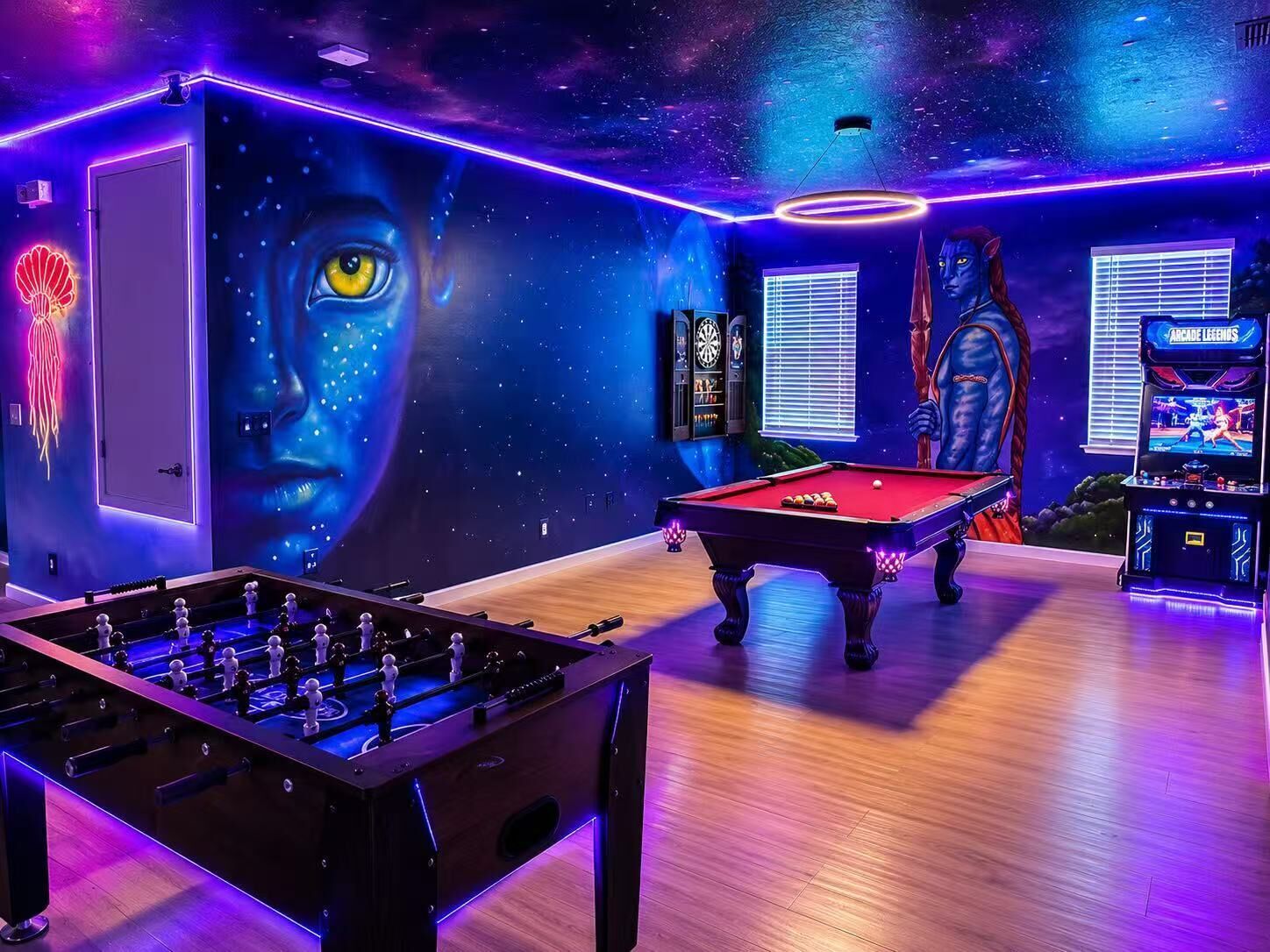 A room with a pool table, foosball table, arcade games, and a mural.