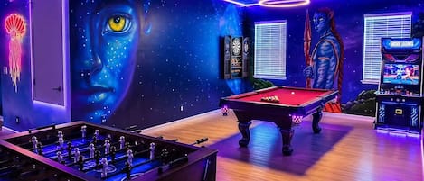 A room with a pool table, foosball table, arcade games, and a mural.