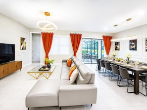 A modern living room with a sofa, coffee table, TV, and dining area with chairs and a table set for a meal. - 36BR Mega Resort  30 Private Suites  Sleeps 80+  Near Disney (kissimmee)