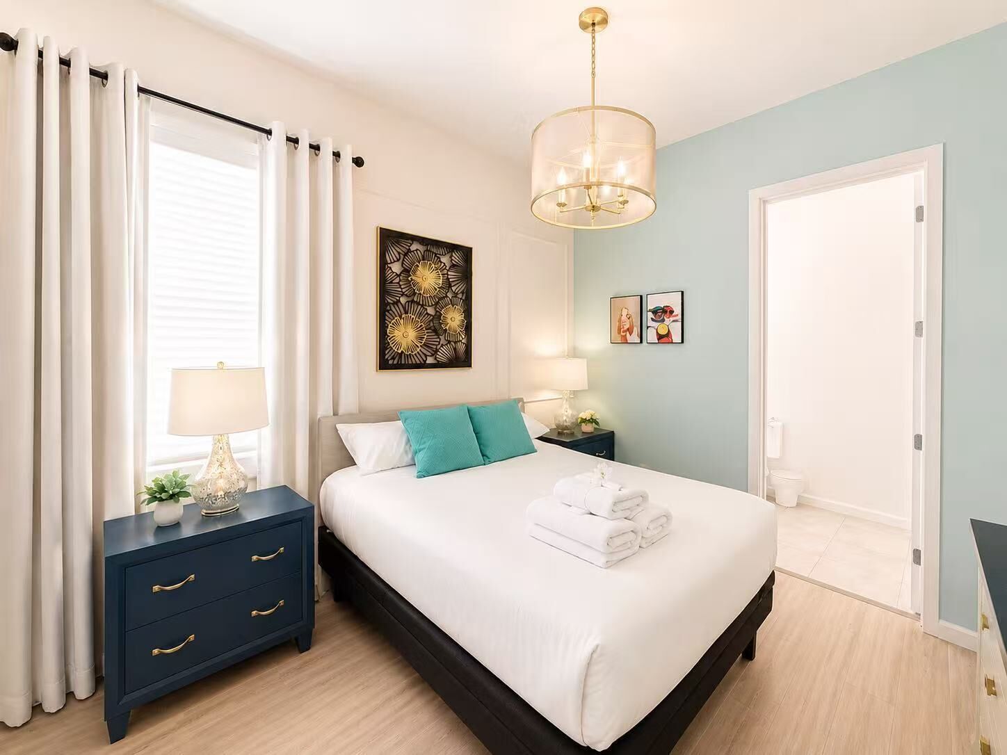 A bedroom with a bed, bedside tables, a nightstand, a wall art piece, and a door.