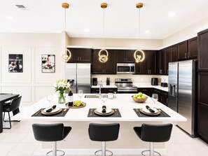 A modern kitchen with dark cabinetry, stainless steel appliances, and a central island with bar stools. - 36BR Mega Resort  30 Private Suites  Sleeps 80+  Near Disney (kissimmee)
