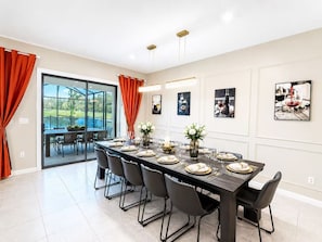 A dining room with a long table set for six, chairs, and a view through a glass door to an outdoor area. - 36BR Mega Resort  30 Private Suites  Sleeps 80+  Near Disney (kissimmee)