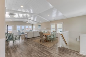 A spacious living area with a wooden ceiling, a dining table with chairs, a sofa, and a view of the outside. - Front Row Paradise | Pool & Ocean Views (Oak Island)