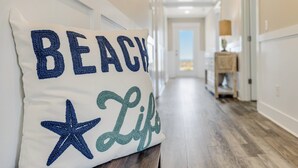Käytävä, jossa on valkoinen seinä, puulattia ja tyyny, jossa on teksti ”BEACH Life”.