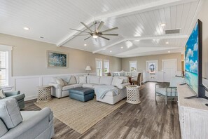 A spacious living room with a ceiling fan, a sectional sofa, a TV, and a dining area. - Front Row Paradise | Pool & Ocean Views (Oak Island)