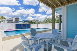 Ein Poolbereich mit weißem Zaun, einem blauen Pool und einer überdachten Terrasse mit weißen Stühlen und einem Tisch.