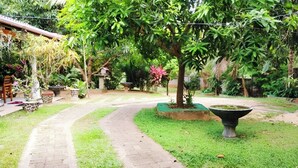 A garden pathway leading to a seating area with a table and chairs, surrounded by lush greenery and a large planter. - Habarana Guest House  (Habarana)