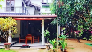 A covered outdoor seating area with a table and chairs, surrounded by potted plants and a staircase leading to a building. - Habarana Guest House  (Habarana)