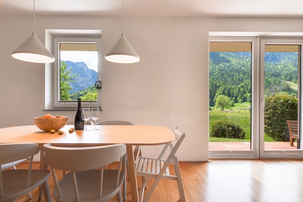 A dining area with a wooden table, white chairs, and a view of a mountainous landscape through large windows.