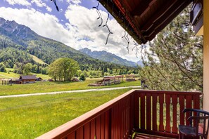 A balcony with a view of a mountainous landscape, a wooden railing, and a chair.