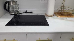 A kitchen with a black induction cooktop, a glass kettle, a paper towel holder, and a gold-colored wire basket. - Haven Serene - Modern, convenient, quiet, private 1 bedroom basement suite (Winnipeg)