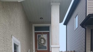 A residential entryway with a concrete pathway leading to a front door, a small window on the left, and a wooden fence in the background. - Haven Serene - Modern, convenient, quiet, private 1 bedroom basement suite (Winnipeg)