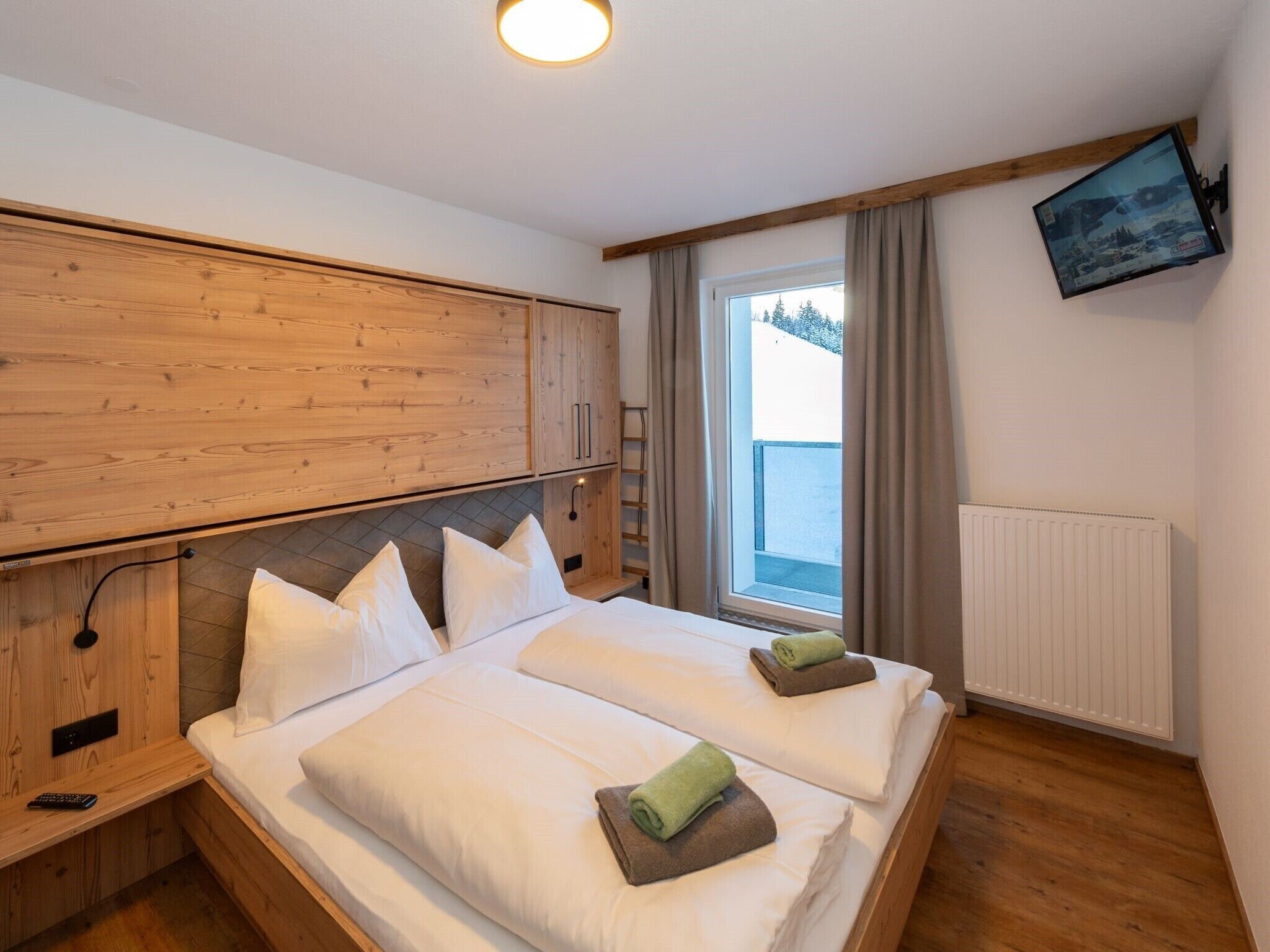 Une chambre d’hôtel avec deux lits, des têtes de lit en bois, un téléviseur fixé au mur et une fenêtre avec des rideaux.
