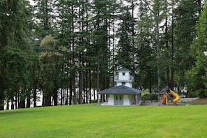 Una cabaña con un edificio principal de dos pisos y una torre separada, rodeada de un bosque denso.