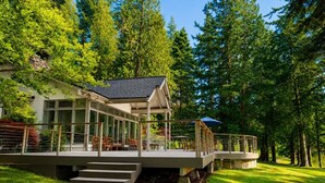 A modern house with a covered patio, outdoor seating, and a stone staircase leading to a deck.
