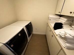A laundry room with two stacked washers and dryers, a white cabinet with towels, and a tiled floor. - Waterfront Main House on 23-Acre Estate (Freeland)