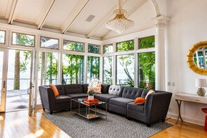 Un salón con un sofá modular, una mesa de centro y ventanas amplias con vistas a árboles.