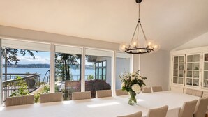 A dining room with a large table and chairs, a chandelier, and a view of a lake.