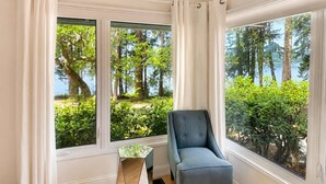 A room with a view of a forest and a lake, a blue chair, and a small table.