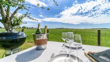 Une table dressée à l’extérieur, avec une bouteille de champagne, des verres et un barbecue.