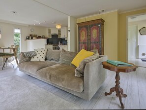 Ein Wohnzimmer mit einer Couch, einem kleinen Holztisch und einer Küche im Hintergrund.