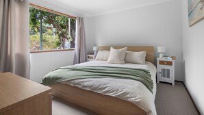 A neatly arranged bedroom with a bed, bedside tables, a desk, and a window with curtains. - Waterfront Creek Access, Large Entertaining Deck, Minutes to Beaches (Hyland Park)
