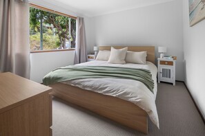 A neatly arranged bedroom with a bed, bedside tables, a desk, and a window with curtains. - Waterfront Creek Access, Large Entertaining Deck, Minutes to Beaches (Hyland Park)