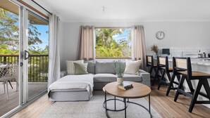 A modern living room with a sofa, a coffee table, and a dining area with chairs. - Waterfront Creek Access, Large Entertaining Deck, Minutes to Beaches (Hyland Park)