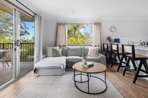 A modern living room with a sofa, a coffee table, and a dining area with chairs. - Waterfront Creek Access, Large Entertaining Deck, Minutes to Beaches (Hyland Park)