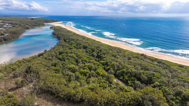 An aerial view of a coastal area with dense forest, a sandy beach, and a clear blue sea. - Waterfront Creek Access, Large Entertaining Deck, Minutes to Beaches (Hyland Park)