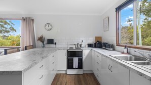 A modern kitchen with white cabinetry, a built-in oven, a coffee machine, and a large window offering a view of greenery. - Waterfront Creek Access, Large Entertaining Deck, Minutes to Beaches (Hyland Park)