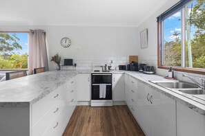 Een moderne keuken met witte kastjes, een ingebouwde oven, een koffieapparaat en een groot raam met uitzicht op groen.