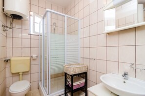Ein Badezimmer mit Toilette, Waschbecken, Dusche mit Glastür und Ablage mit Korb.