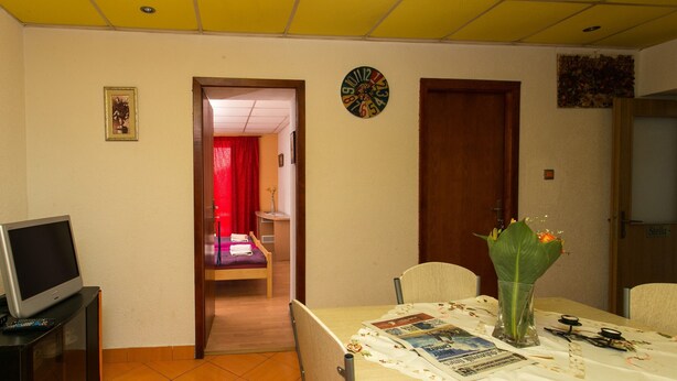 Zona pranzo con tavolo, sedie, un vaso con fiori, una sveglia e una televisione su un mobile.