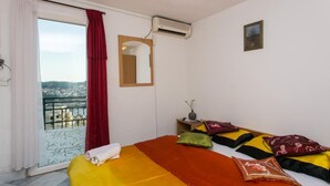 Una camera d'albergo con un letto, una finestra con tende, un condizionatore d'aria, un tavolino con un vaso e vista sulla città.