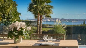Uma mesa de jantar posta com pratos, copos e talheres, com vista para uma paisagem cênica de um corpo d'água e edifícios ao longe.