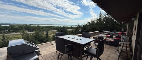 An outdoor patio with a table and chairs, a grill, and a view of the landscape.
