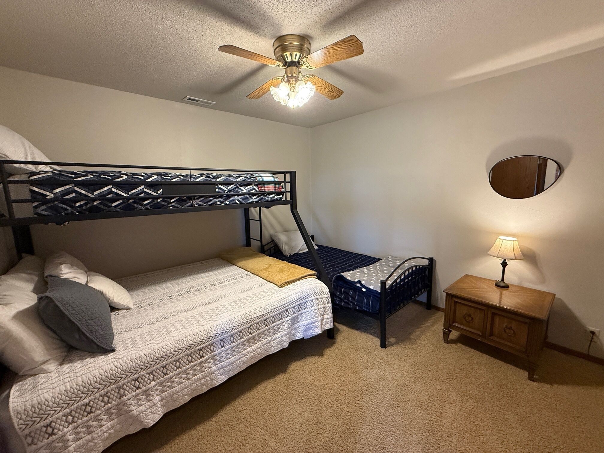 Habitación con literas, un ventilador de techo, una mesita de noche con lámpara y un espejo en la pared.