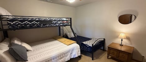 Habitación con literas, un ventilador de techo, una mesita de noche con lámpara y un espejo en la pared.