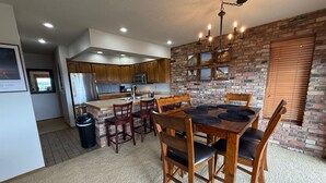 Una cocina con armarios de madera, una mesa de comedor con sillas, una araña y una pared de ladrillo.