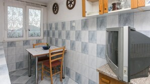 Uma cozinha com uma mesa de jantar, cadeiras, uma televisão e uma janela com cortinas.