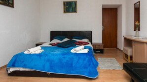Um quarto com uma cama, mesa de cabeceira, escrivaninha, cadeira, espelho e porta.