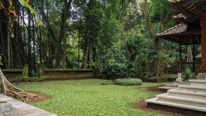 Un jardín con un banco de piedra, un pequeño estanque y un pabellón.