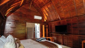 Una habitación de cabaña de madera con una cama, almohadas, un televisor y un armario de madera.