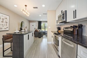 A modern kitchen with stainless steel appliances, a central island, and a dining area with a sofa. - Cozy home in dwtn + 6 guests! (Orlando)