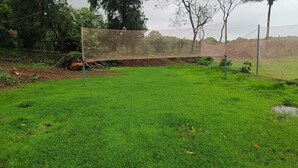 Uma área externa com gramado, cercada por uma rede, árvores e uma cerca.