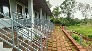 A building with a staircase leading to a covered area, surrounded by greenery. - Beaches & Hills Resorts (Shrivardhan)